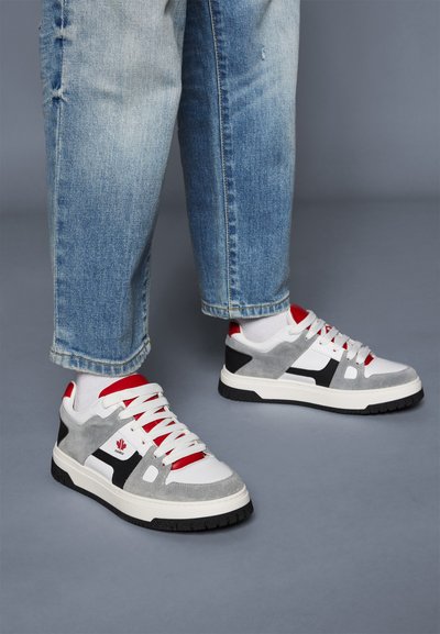 Sneaker bianchi e grigi con accenti neri, lacci rossi e una finitura in suede testurizzato. La suola ha una presa in gomma nera, con un dettaglio del logo.