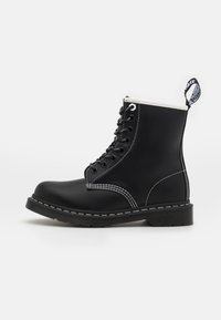Černá kožená kotníková bota s bílým prošíváním, kulatou špičkou, šněrováním vpředu a zesílenou patou. Disponuje poutkem na límci.