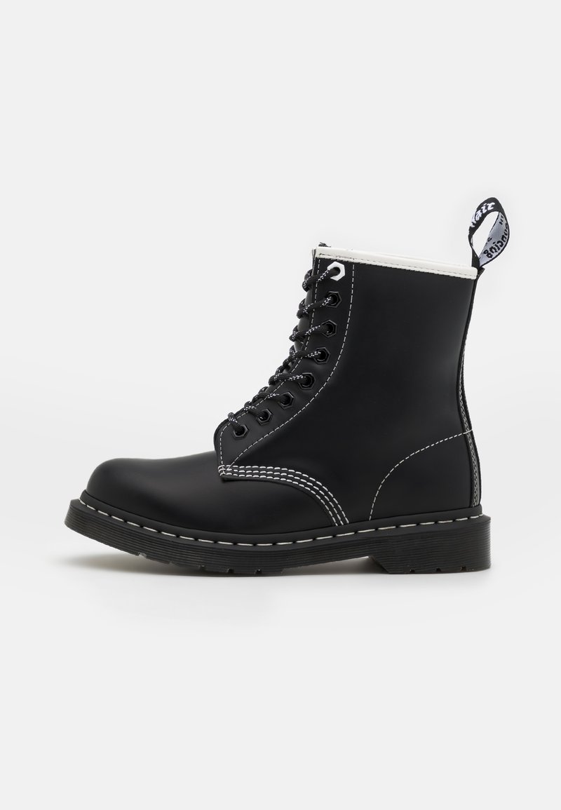 Černá kožená kotníková bota s bílým prošíváním, kulatou špičkou, šněrováním vpředu a zesílenou patou. Disponuje poutkem na límci.