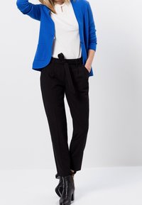 Cárdigan azul, blusa blanca con escote en forma de llave, pantalones negros con cintura con lazo y botas negras hasta el tobillo. Texturas suaves y diseño ajustado en todo.