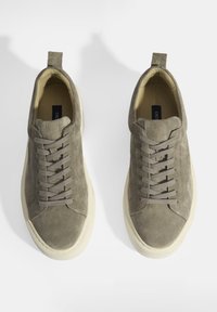 Grey suede sneakers with a low-top design, round toe, flat laces, and a rubber outsole. Features a rear pull tab for easy wear.