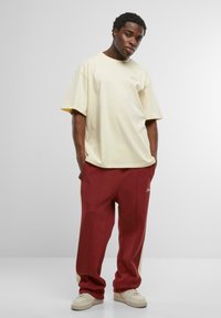 Lichtgele, oversized t-shirt met logo, gecombineerd met donkerrode joggers met zijpanelen en een getailleerde pasvorm. Witte sneakers maken de look compleet.