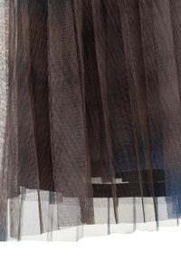 Durchsichtiger schwarzer Tüllstoff, der über einem dunklen Rock geschichtet ist und die Textur sowie die durchscheinende Qualität des Materials zeigt.