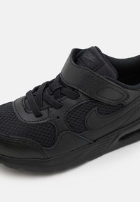 Svarta Nike-sneakers med en blandning av slätt läder och mesh-texturer, kardborreband, snörning och en synlig luftdämpningsenhet.