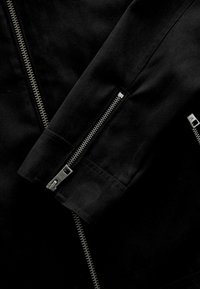Black jacket featuring silver zippers, with a smooth texture. The design includes a close-up view of the sleeve and zipper details.