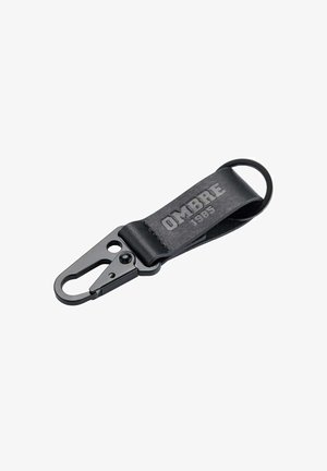 Porte-clés en cuir noir avec clip en métal, présentant le texte en relief "OMBRE" et "1985", texture lisse et attache en boucle pour les clés.
