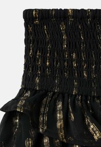 Čierna smockovaná látka s akcentami z kovovej zlatej pruhy, s volánom na spodnom leme. Textúra vyzerá mäkko a elasticky.