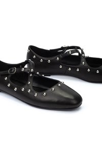 Bailarinas de cuero negro con correas cruzadas, adornadas con tachuelas plateadas en la parte superior, con puntera puntiaguda y suela plana.