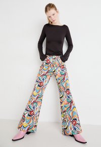Top nero a maniche lunghe, pantaloni svasati a fantasia con swirl multicolori e décolleté a punta rosa. Tessuto liscio e design aderente.
