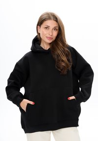 Felpa nera oversize con tasca a marsupio, polsini e orlo a costine. Tessuto morbido, cappuccio con cordino, e vestibilità rilassata per un comfort ottimale.