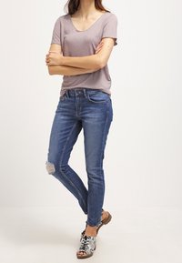 Grå V-hals t-shirt i kombination med blå skinny jeans med slitna knän. Skorna består av bruna sandaler med ormskinnsmönster.