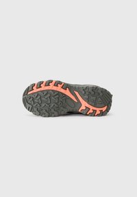 Semelle en caoutchouc noire et orange d'une chaussure de randonnée avec un profond relief pour une meilleure traction sur un fond clair.