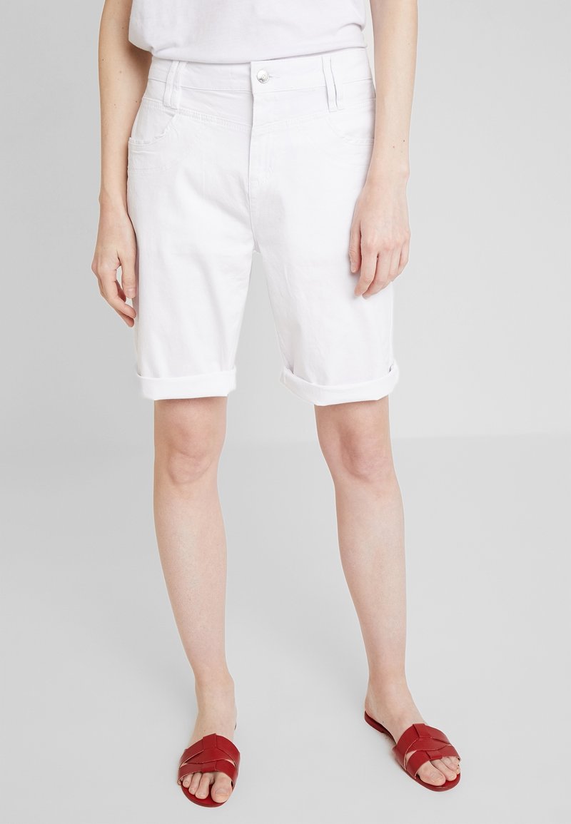 Shorts en denim blanc avec des ourlets roulés, design à cinq poches et fermeture par bouton supérieur. Texture lisse et coupe standard. Associés à des sandales à glisser rouges.