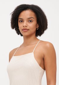 Satin topp i lys beige med teksturert overflate. Har tynne stropper og en glitrende paljett-detail på den ene siden.