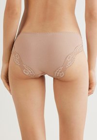 Beige geribde slipjes met florale kantafwerking aan de zijkanten, met een lage taille en een gladde textuur.