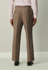 Braune karierte Hose mit geradem Schnitt, strukturiertem Stoff, Gesäßtaschen und Bügelfalte entlang der Beine, kombiniert mit schwarzen Schuhen.