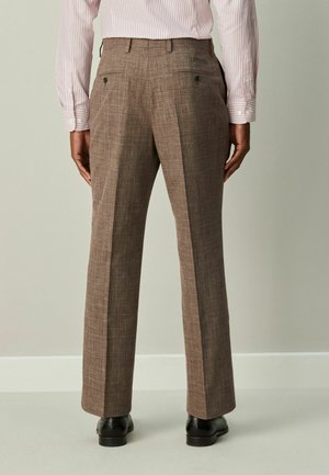 Brown plaid trousers with a straight fit, textured fabric, back pockets, and a crease down the legs, paired with black shoes.