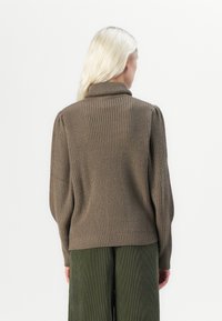 Brun, ribbad stickad tröja med hög krage och puffärmar, i kombination med mörkgröna vida byxor. Texturerad, avslappnad passform.