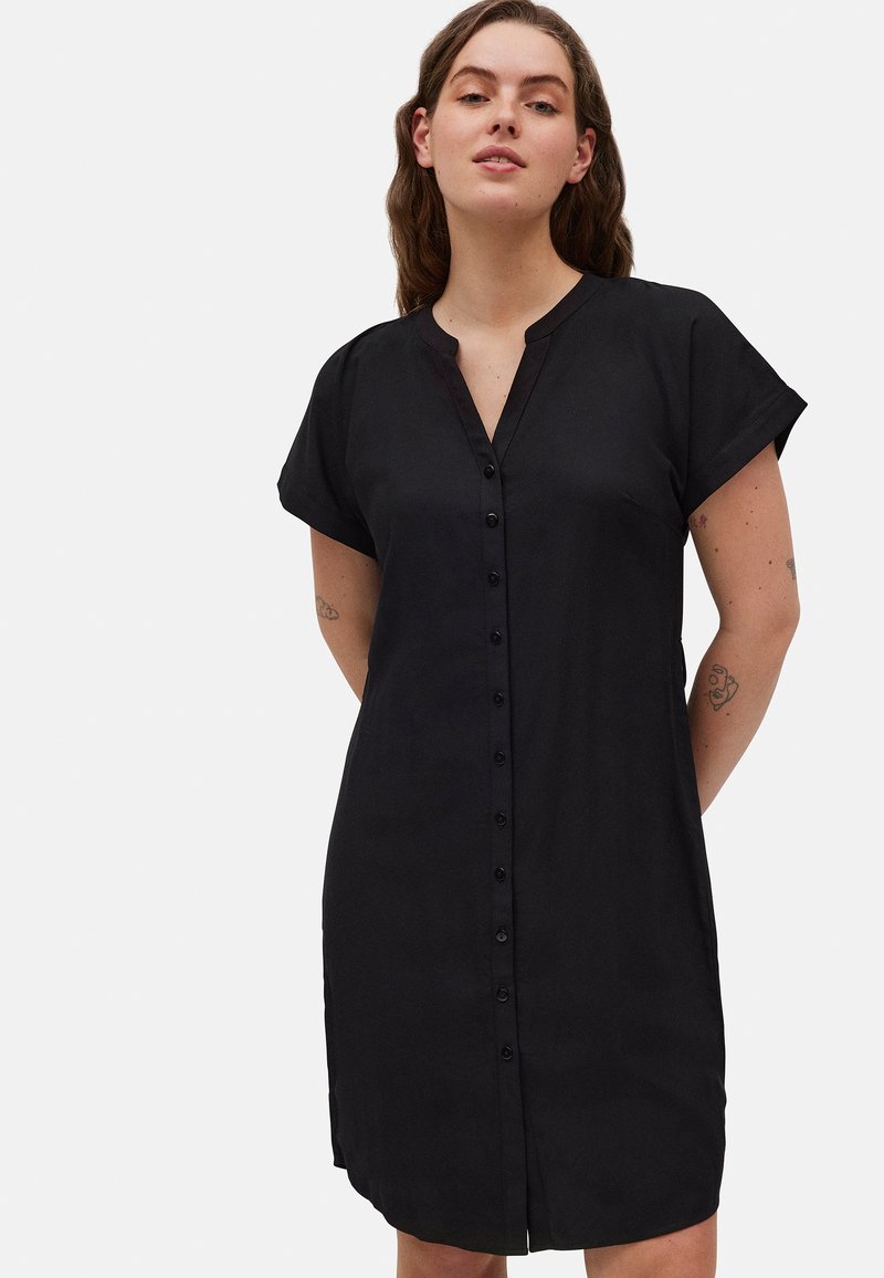 Vestido negro de camisa hecho de una tela suave, con un cierre de botones en la parte delantera, mangas cortas, un cuello tipo mandarín y aberturas laterales para facilitar el movimiento.