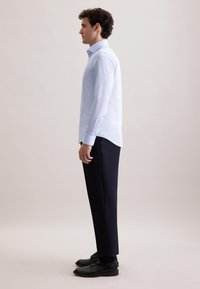 Lichtblauwe overhemd met lange mouwen en een normale kraag, gecombineerd met marineblauwe broeken en zwarte schoenen, zijaanzicht.