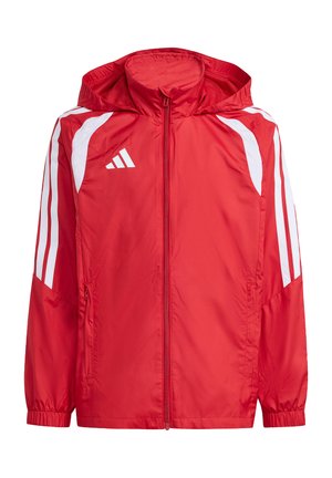 Junge Person trägt eine rote Sportjacke mit Reißverschluss, weißen Streifen und Kapuze, kombiniert mit schwarzen Hosen mit weißem Logo.