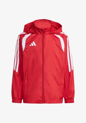 Junge Person trägt eine rote Sportjacke mit Reißverschluss, weißen Streifen und Kapuze, kombiniert mit schwarzen Hosen mit weißem Logo.