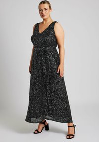 Vestido maxi negro sin mangas con escote en V, adornado con lentejuelas dispersas para dar textura. Incluye un detalle de lazo en la cintura.