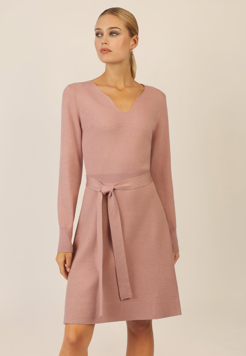 Strickkleid in sanftem Pink mit V-Ausschnitt, langen Ärmeln und Taillengürtel. Bietet eine lockere Passform und gerippte Akzente an den Bündchen und dem Saum.