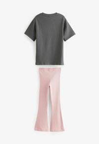 T-shirt en coton gris à manches courtes et encolure ronde, associé à un pantalon à pattes d'éléphant côtelé rose clair. Texture uniforme sur l'ensemble.