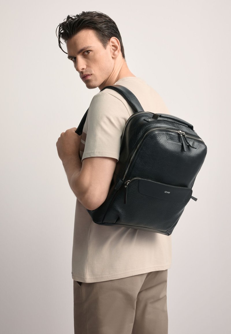 Czarny skórzany plecak o uporządkowanym kształcie, z zamykanymi na zamek kieszeniami i przednią kieszenią. Teksturowane wykończenie i regulowane paski.