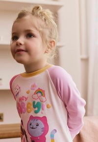Langarmshirt für Kinder mit einem weißen Körper und rosa Ärmeln. Mit einem bunten Grafikdesign, das Cartoonfiguren, Herzen und ein Regenbogenmuster zeigt.
