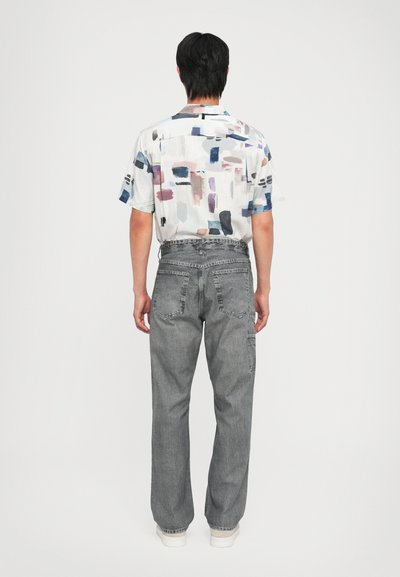 Kortermet skjorte med et flerfarget abstrakt mønster, kombinert med løse grå denimjeans med baklommer og en falmet tekstur.