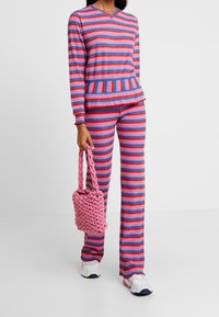 Prążkowany zestaw dzianinowy do wypoczynku w kolorach różowym, niebieskim i czerwonym. Bluzka z dekoltem w serek, spodnie o szerokich nogawkach. Do zestawu dołączona różowa pleciona torebka.