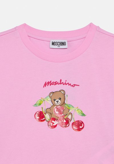 Ροζ βαμβακερό μπλουζάκι με στρογγυλή λαιμόκοψη, με απεικόνιση αρκούδας ανάμεσα σε κεράσια. Λογότυπο "Moschino Kid" σε κόκκινο πάνω από το σχέδιο.