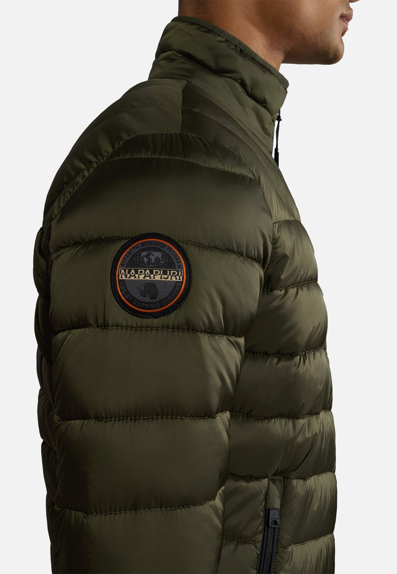 Oliwkowa kurtka puchowa z wysokim kołnierzem, poziomym przeszyciem, bocznymi kieszeniami na zamek i okrągłą naszywką z logo na górnej części rękawa.