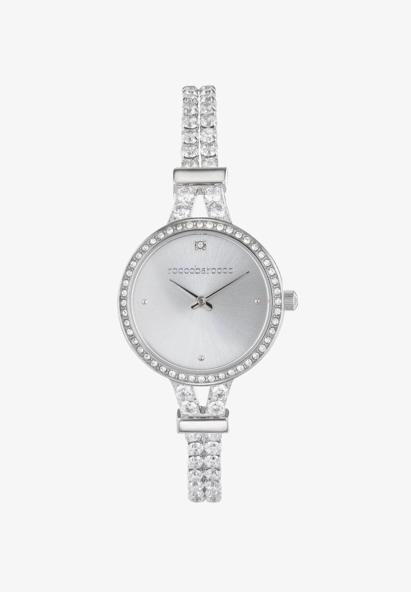 Srebrna ura za zapestje s gladkim okroglim obrazom, iskrivi kristalni dodatki in dvojnim pasom z rhinestones. Eleganten minimalističen dizajn.