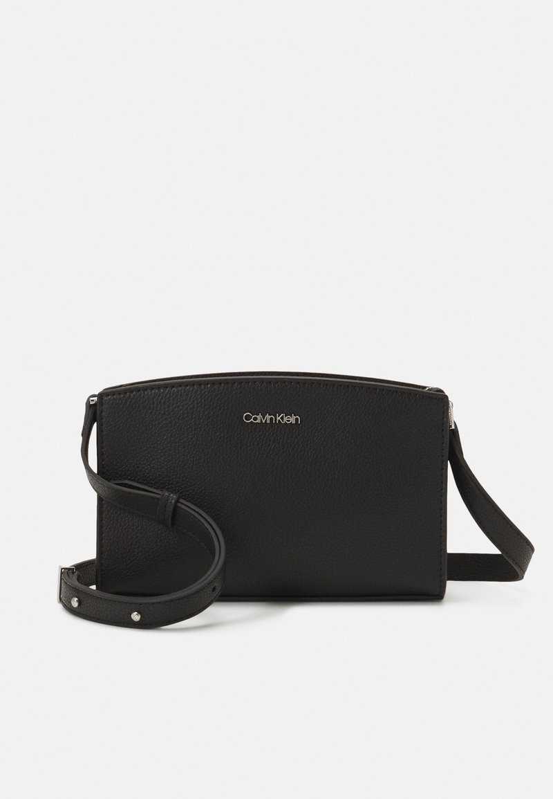 Schwarze Leder-Crossbody-Tasche mit strukturierten Oberflächen, Reißverschluss und verstellbarem Tragegurt mit metallischen Akzenten. Markenlogo auf der Vorderseite angezeigt.