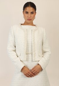 White textured jacket with pearl accents and embedded sequins, featuring a cropped design and long sleeves, paired with a matching dress.