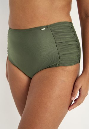 Nahaufnahme einer Person, die olivgrüne, hochtaillierte Badeshorts mit gerafften Seitenpaneelen und einem kleinen metallischen Logo vorne trägt.