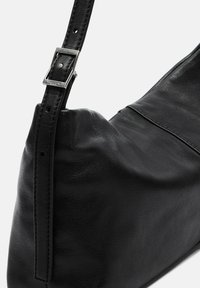 Zwarte leren handtas met een curvy vorm, een gestructureerd oppervlak en een verstelbare schouderband met een metalen gesp.