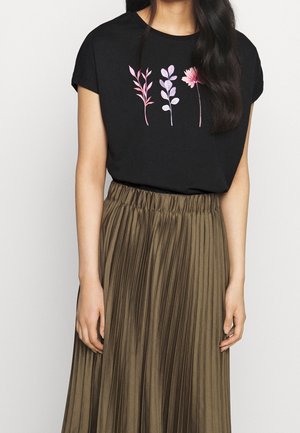 Femme portant un t-shirt noir à manches courtes avec des imprimés floraux roses et une jupe plissée taille haute vert olive.