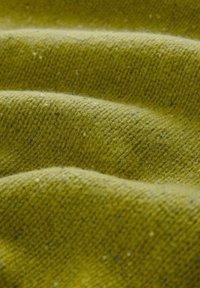 Nahaufnahme eines strukturierten senfgelben Stoffes mit feinem Strickmuster und sichtbaren kleinen Fasern und Flecken.