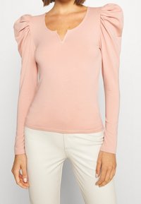 Långärmad topp med puffärmar i mjuk rosa tyg. Har en V-ringning och en figurnära design, med rynkade detaljer på ärmarna.