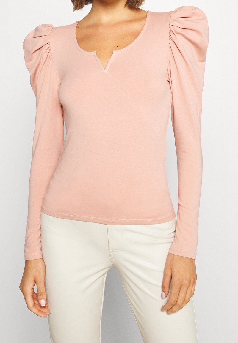 Långärmad topp med puffärmar i mjuk rosa tyg. Har en V-ringning och en figurnära design, med rynkade detaljer på ärmarna.