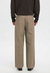 Beige bukser med vidde i benene, lavet af bomuld med en glat tekstur. Har to baglommer og en skræddersyet pasform. Bæres med en mørk sweater.