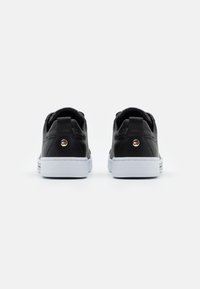 Ein Paar schwarze Low-Top-Sneaker mit weißen Sohlen, von hinten präsentiert, mit einem kleinen runden Logo an jeder Fersenschlaufe.