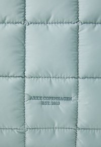 Világos türkiz szövet, párnázott felülettel, steppelt mintával. A felső részén "ARKK COPENHAGEN EST. 2015" felirattal, kiemelő varrással. 