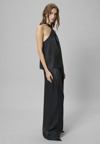 Top halter in satin nero con dettaglio al collo da annodare, abbinato a pantaloni a gamba larga in satin nero che creano una silhouette elegante e fluida.