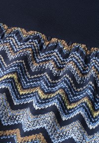 Motif zigzag ondulé sur tissu avec des couleurs bleu marine, bleu clair, beige et blanc sous une bande côtelée bleu foncé unie.