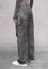 Zwarte en grijs vervaagde denim cargobroek met een losse pasvorm, zijzakken en opvallende stikdetails, gecombineerd met witte sneakers.